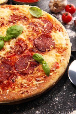 İtalyan pizza salam, peperoni - eritilmiş peynir, kırmızı domates ve peynir, domates ve kırmızı kiraz domates tarafından dekore edilmiş bir tabloda yeşil fesleğen ile