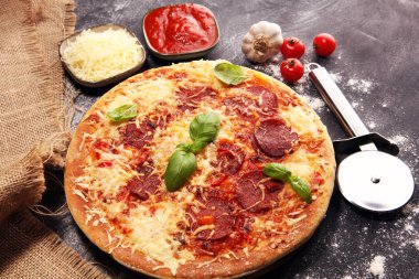 İtalyan pizza salam, peperoni - eritilmiş peynir, kırmızı domates ve peynir, domates ve kırmızı kiraz domates tarafından dekore edilmiş bir tabloda yeşil fesleğen ile