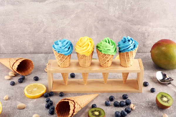 Vanilla frozen yogurt or soft ice cream in waffle cone. Diffrent flavor ice cream with kiwi and pistachio, mango and lemon, blueberry and blackberry