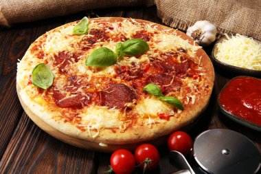 İtalyan pizza salam, peperoni - eritilmiş peynir, kırmızı domates ve peynir, domates ve kırmızı kiraz domates tarafından dekore edilmiş bir tabloda yeşil fesleğen ile