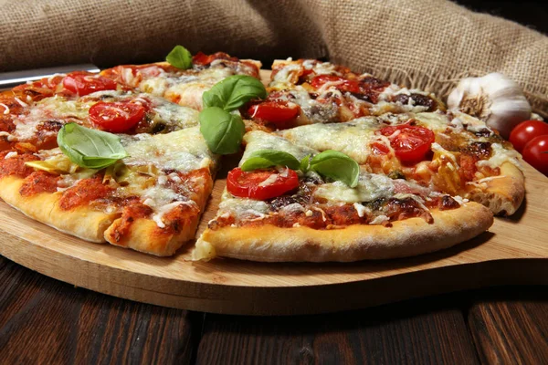 Vegetarian Italian pizza with melted cheese, red tomatoes and green basil on a table decorated by cheese, tomato and red cherry tomatoes
