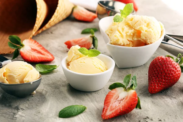 Vanilla ice cream scoop with fresh strawberries and icecream cones on a rustic background