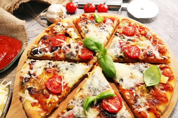 Vegetarian Italian pizza with melted cheese, red tomatoes and green basil on a table decorated by cheese, tomato and red cherry tomatoes