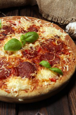 İtalyan pizza salam, peperoni - eritilmiş peynir, kırmızı domates ve peynir, domates ve kırmızı kiraz domates tarafından dekore edilmiş bir tabloda yeşil fesleğen ile