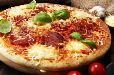 İtalyan pizza salam, peperoni - eritilmiş peynir, kırmızı domates ve peynir, domates ve kırmızı kiraz domates tarafından dekore edilmiş bir tabloda yeşil fesleğen ile