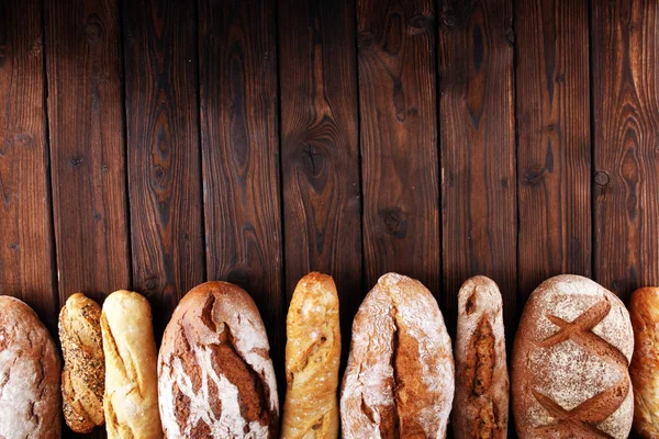 Sült kenyeret és zsemlét, a háttérben fából készült asztal — Stock Fotó