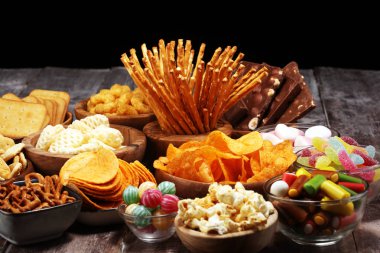 Salty snacks. Pretzels, chips, crackers in wooden bowls on table clipart