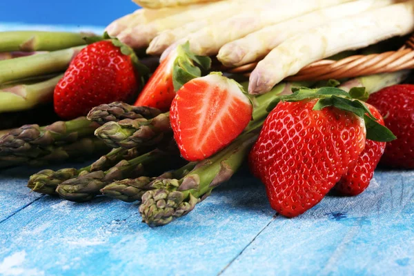 White and green asparagus with strawberries on wood