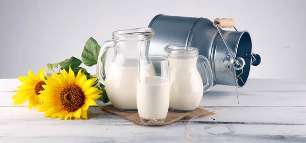 Een kruik melk en glas melk op een houten tafel en bloem — Stockfoto