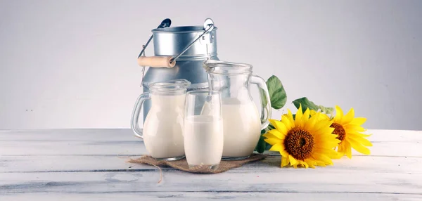 Una jarra de leche y un vaso de leche sobre una mesa de madera y una flor —  Fotos de Stock