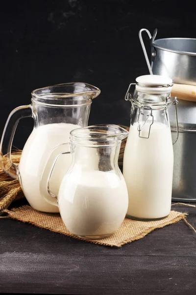 Una brocca di latte e un bicchiere di latte su un tavolo nero di legno — Foto Stock