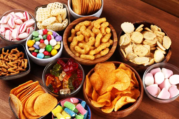 Соленые закуски. Крендельки, чипсы, крекеры и сладости на столе — стоковое фото