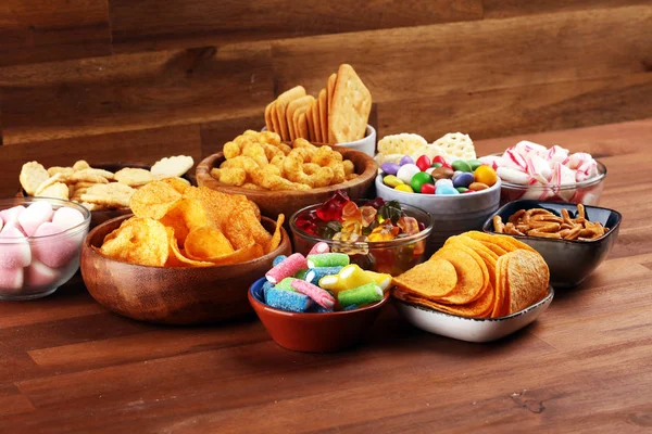 Petiscos salgados. Pretzels, batatas fritas, biscoitos e doces na mesa — Fotografia de Stock