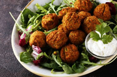 Arka planda sarımsaklı yoğurt soslu nohut köftesi.