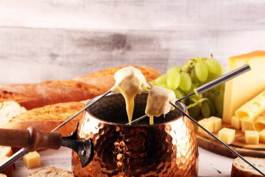 Bir kış akşamı gurme İsviçre fondü yemeği tahtanın üzerinde çeşitli peynirlerle birlikte çatallı ve peynirli fondü. 