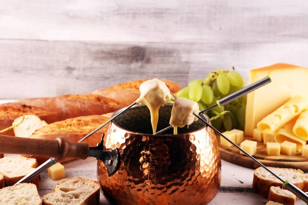 Bir kış akşamı gurme İsviçre fondü yemeği tahtanın üzerinde çeşitli peynirlerle birlikte çatallı ve peynirli fondü. 