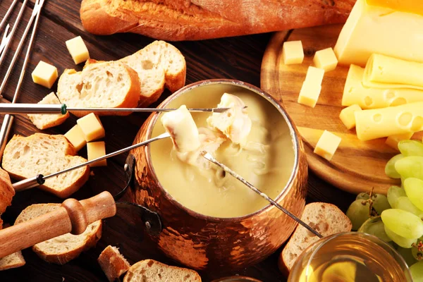 Bir kış akşamı gurme İsviçre fondü yemeği tahtanın üzerinde çeşitli peynirlerle birlikte çatallı ve peynirli fondü. 