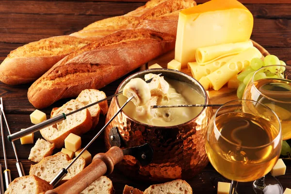 Bir kış akşamı gurme İsviçre fondü yemeği tahtanın üzerinde çeşitli peynirlerle birlikte çatallı ve peynirli fondü. 