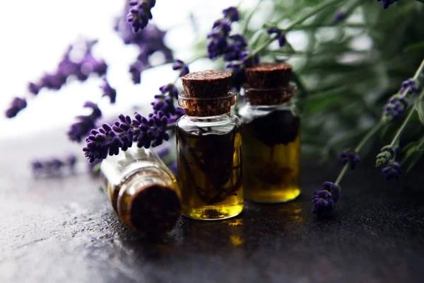Masadaki taze çiçeklerin arka planında cam şişedeki lavanta yağı.