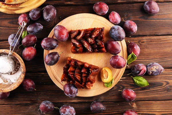 Rustic plum cake on wooden background with plums around. Plum pie concept