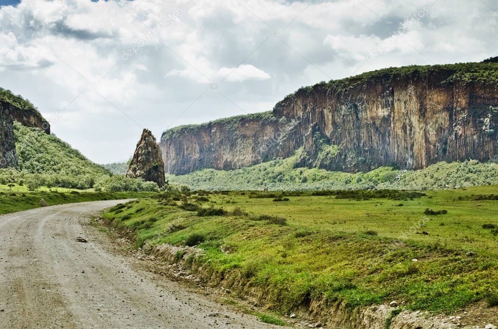 scenic view of dirt road with cliffs and lush greenery under cloudy sky