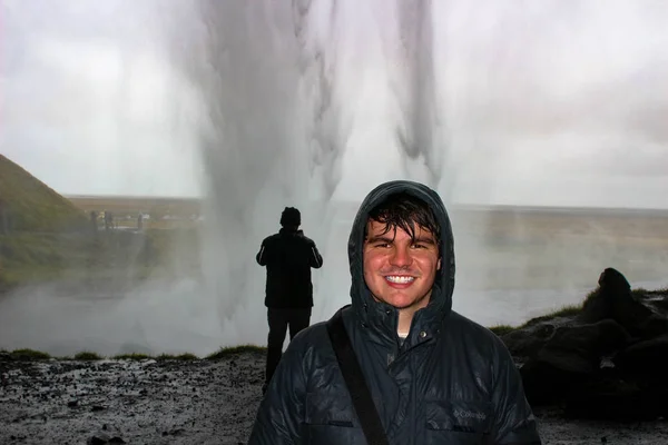 Erkek turist buz içinde çok ıslak bir sahnede bir şelale arkasında pozlar — Stok fotoğraf