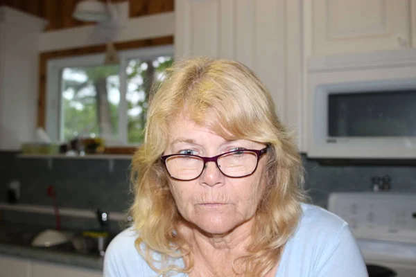 Close-up attente middelbare leeftijd blonde vrouw, zittend in de woonkamer en kijken met de handen op de kin. — Stockfoto