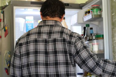 Buzdolabında yiyecek bakarak karışık bir genç adam arkadan görünüş