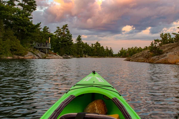 Kayak en aguas tranquilas y tranquilas hacia la puesta de sol. Disparo desde el punto de vista del remador . — Foto de Stock