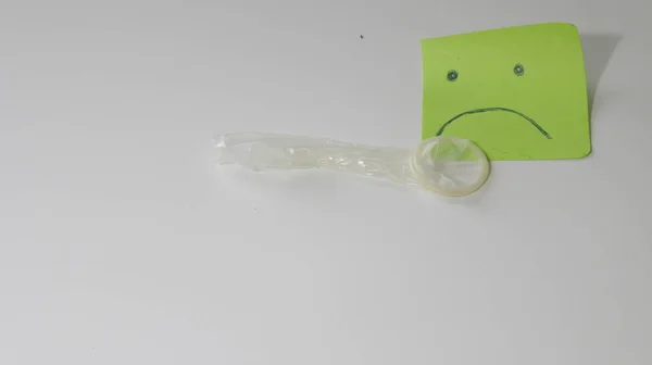Kondom bredvid en fästis med ett sorgset ansikte, begreppet infertilitet — Stockfoto