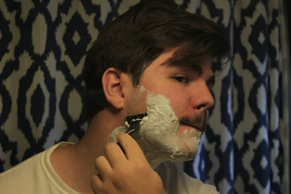 Mann zwischen 18 und 25 Jahren rasiert sich im Spiegel — Stockfoto