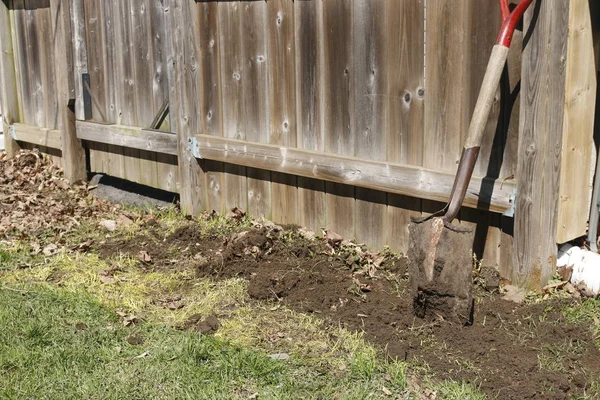 This rusty shovel has seen years of use. It leans against a red fence. — Stock Photo, Image