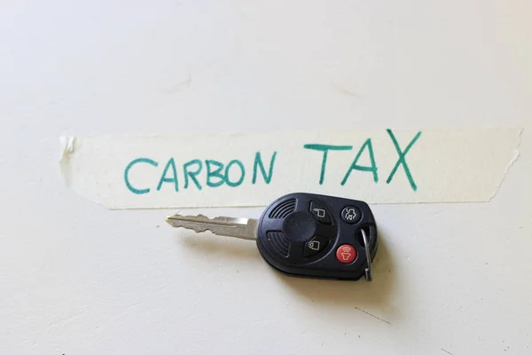 Een autosleutel naast een notitie die zegt Carbon Tax. concept van het verhogen van de kosten voor de aandrijving of de problemen met een koolstofbelasting. — Stockfoto