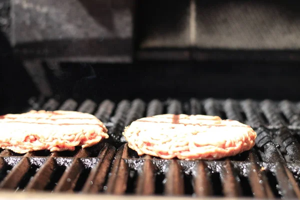 Ωμό μπέργκερ σε μπάρμπεκιου ψησταριά με φωτιά. Κρέας φαγητού-ωμό μπέργκερ σε ψησταριά μπάρμπεκιου με φωτιά. Τα ρηχά — Φωτογραφία Αρχείου