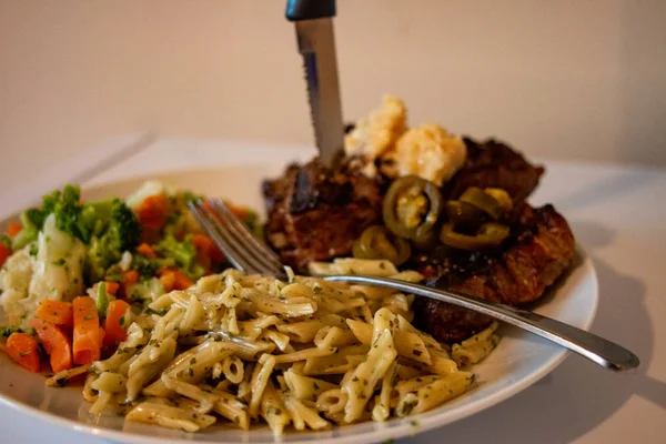 Közeli kilátás egy tányér szűzpecsenyét steak, közepes ritka, tálalva tészta és zöldség fehér háttér — Stock Fotó