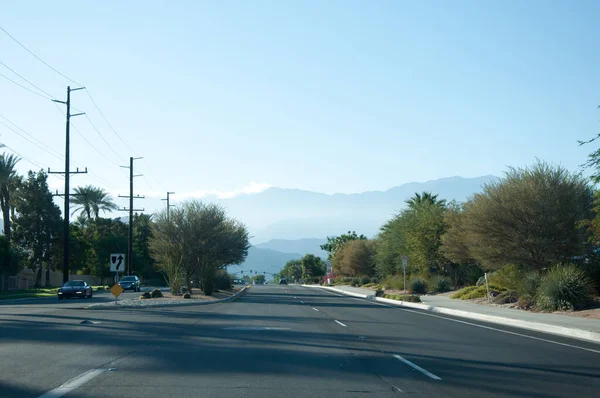 Rader av palmer, berg, blommor, blå himmel och öppna vägar, Kalifornien Palm Springs. — Stockfoto