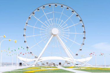 Beyaz dönme dolap cazibesi. Renkli lambalar, parlak çiçekler ve yeşil çimenler.