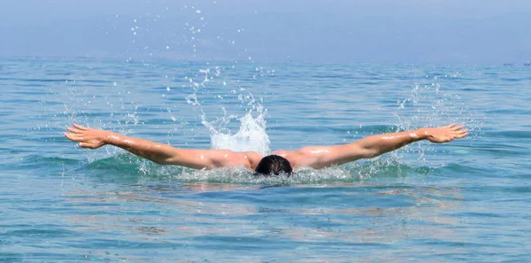 Muskulöser junger Mann schwimmt Schmetterlingsstilen — Stockfoto