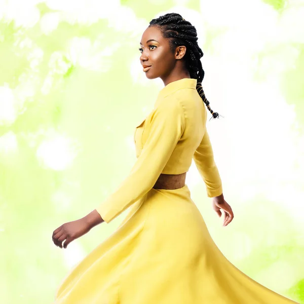 关闭工作室肖像的年轻迷人的非洲妇女穿着黄色礼服 女孩与编织的发型摇摆丝绸礼服反对多彩的绿色背景 — 图库照片