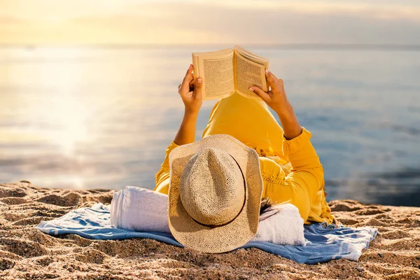 草帽子的年轻妇女在日落读书书 — 图库照片
