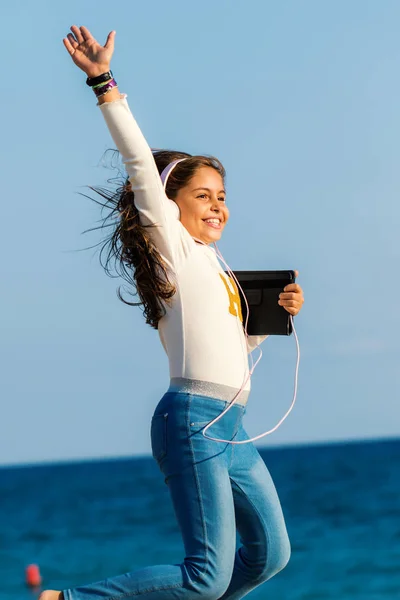 Close Action Portrait Smiling Tween Girl Jumping Headphones Tablet Beach — Stock Photo, Image