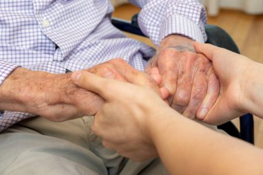 Genç kadın caregiver yakın yukarı detay tekerlekli sandalye yaşlı adam ile eller tutarak.