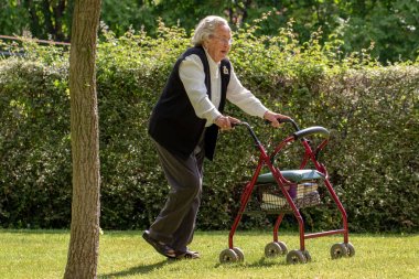 Bahçede tıbbi Rolling Walker ile yürüyen kıdemli kadının tam uzunlukta portre.