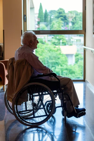 坐在轮椅上的孤残老人的全长画像 面对背光 老人盯着窗户 — 图库照片