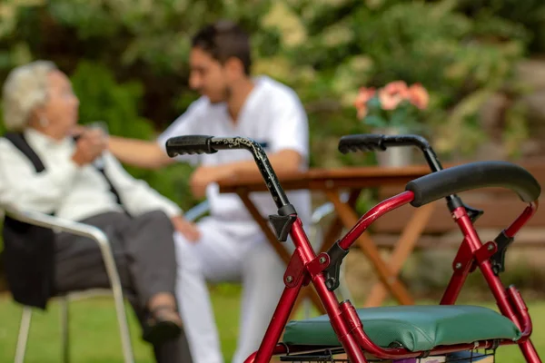 Close up detail of adult walker with old lady and young male assistant in uniform in background. Two people out of focus.