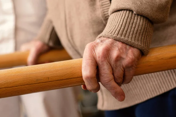 Extreme close up detail of aged human hands grabbing parallel rehabilitation bars.