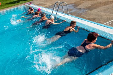 Group of senior women doing exercises in outdoor pool. Elderly ladies kicking with legs in water. clipart