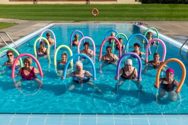 Front view portrait of senior aqua gym class with foam noodles. Sportive ladies standing together in outdoor swimming pool. clipart