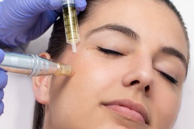Kozmetik mezoterapi yüz olan genç kadın yakın. Terapist yanak derma kalem ile ilaç enjekte.