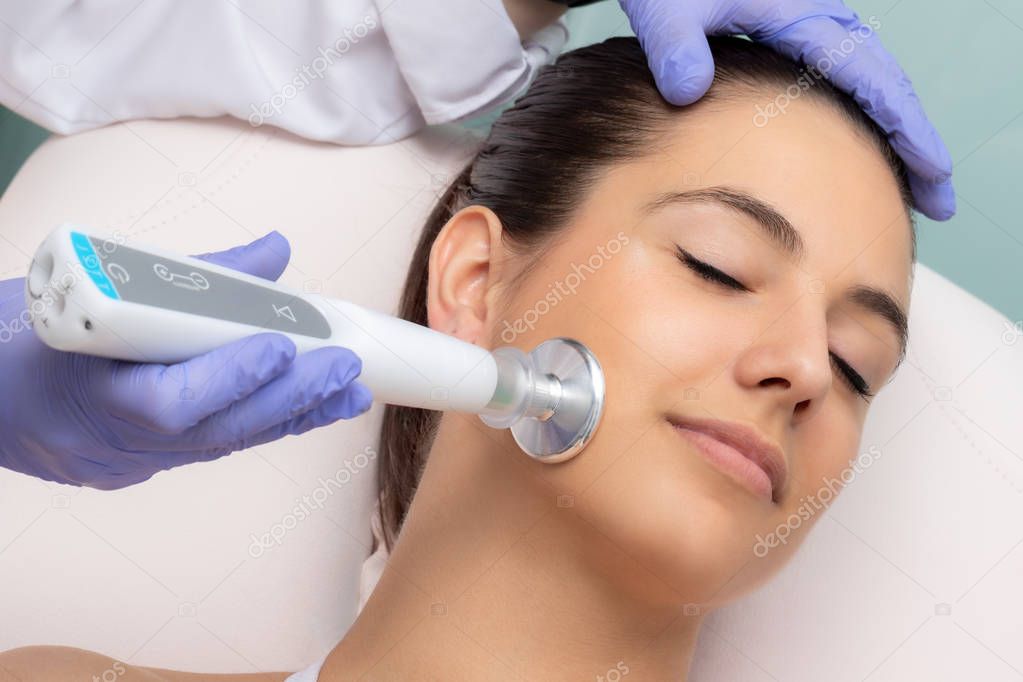 Close up of therapist doing facial mesotherapy treatment with flat head plasma pen. Electric impulse on woman's cheek stimulating new collagen.